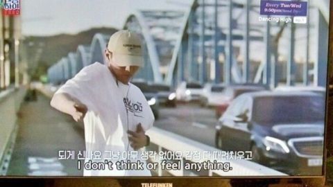 Ein Mann steht an einer Brücke und zieht sein T-Shirt hoch, während ein Auto vorbeifährt. Auf dem Bildschirm steht: "I don't think I'll feel anything."