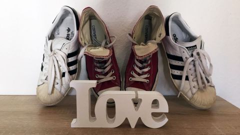 Weiße und rote Sneakers stehen nebeneinander auf einem Tisch, während eine Holztrophäe mit dem Wort "Love" im Vordergrund platziert ist.