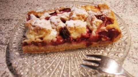 Ein saftiger Zwetschgenkuchen liegt auf einem gläsernen Teller und wird von einer Gabel begleitet, um ihn zu genießen.