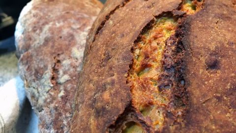 Frisches (Kürbis)-Urdinkelbrot mit knuspriger Kruste liegt auf einem Tablett in einer hellen Küche.