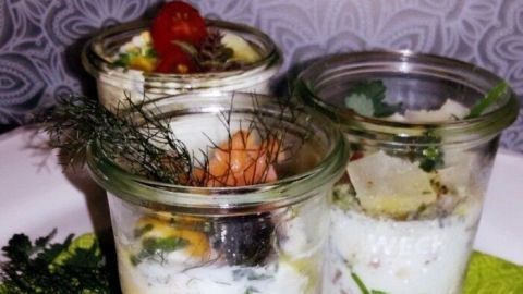 Ein Weckglas enthält ein Frühstücksei, das auf einer grünen Serviette neben Brotscheiben und Kräutern platziert ist.