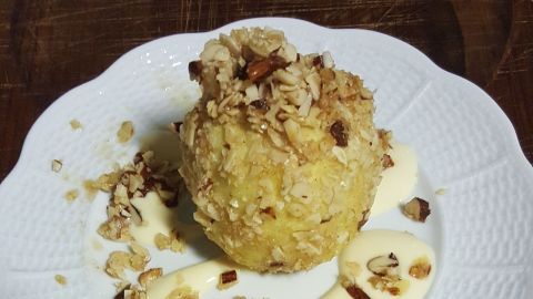 Auf einem weißen Teller liegt ein Bratapfel, der mit Nüssen bestreut und von einer Sahnesauce umgeben ist.