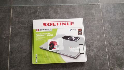 Eine digitale Personenwaage liegt auf einem grauen Fliesenboden, bereit zur Nutzung zur Unterstützung von Ess- und Trinkgewohnheiten.