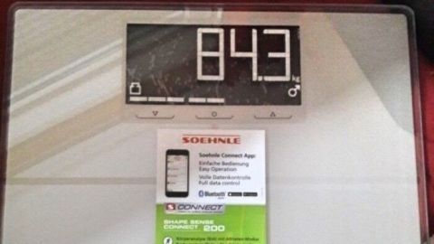 Eine digitale Waage zeigt das Gewicht von 84.3 kg an, umgeben von einem roten Untergrund, ideal für gesundes Entwässern.