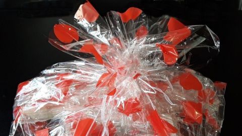 Ein Geschenk ist in durchsichtiger Folie mit roten Herzchen eingewickelt und auf einer schwarzen Oberfläche platziert.