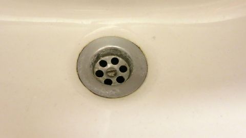 Ein verchromter Abfluss im Waschbecken zeigt eine mögliche Verstopfung, die mit einem Kompressor gereinigt werden kann.