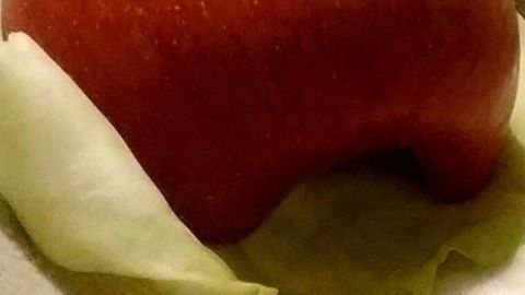 Ein roter Apfel liegt auf frischen Kohlblättern in einer geschützten Umgebung, bereit zum Verzehr oder zur Präsentation.