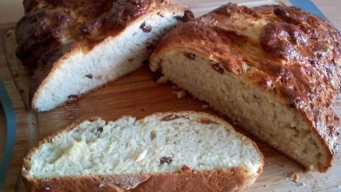 Ein frisch gebackener Hefezopf mit Rumrosinen und Mandeln liegt auf einem Holzbrett, während ein Stück davon bereits geschnitten ist.