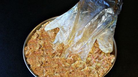 Übergroße Plastikhandschuhe liegen über einer Schüssel mit einer Mischung, ideal für hygienisches Arbeiten in der Küche.