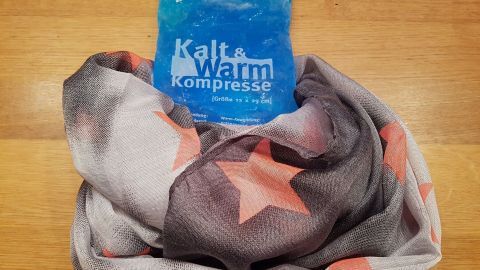 Ein blaues Kühlpaket liegt auf einem bunten Tuch, bereit zur Linderung von Schwellung und Rötung nach einer Impfung.
