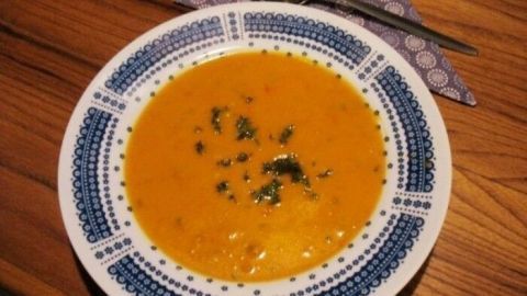 Eine cremige Kürbis-Karotten-Suppe mit einer glatten Konsistenz liegt in einer dekorativen Schüssel auf einem Holztisch.