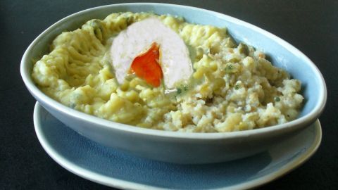 Ein Teller mit cremigem Kartoffelpüree, garniert mit einem pochierten Ei und einer süßsauren Soße in einem blauen Behälter.