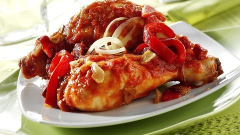 Ein Hähnchengericht mit Paprika und Zwiebeln, serviert auf einem weißen Teller, umgeben von frischem Grün.