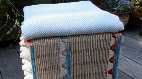Ein Hocker aus Eierkartons steht auf einemHolzboden, dekoriert mit einer Decke, umgeben von Pflanzen im Freien.