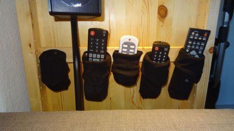 Schwarze Socken hängen an einer Holzwand und halten mehrere Fernbedienungen, die ordentlich verstaut sind.