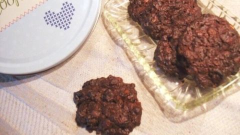 Dunkle, fruchtige Schoko-Nugat-Cookies liegen auf einem Tablett, während eine bunte Dose mit "Cookies" daneben steht.