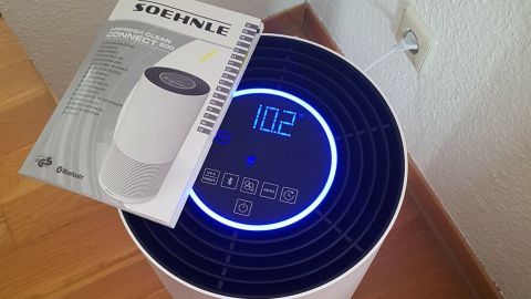 Ein Luftreiniger steht auf dem Holzfußboden und zeigt 102 auf dem Bildschirm an, um Staub in der Wohnung zu reduzieren.