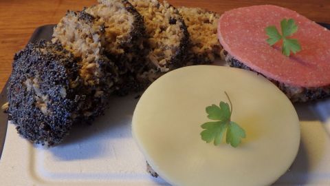 Tassenbrot mit Flohsamenschalen liegt auf einem Teller, umgeben von Scheiben Käse und Wurst, garniert mit Petersilie.