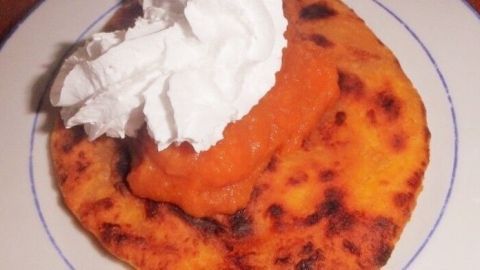 Eine goldbraune Möhrenpfannkuchen liegt auf einem Teller, garniert mit einer Portion Möhrenkaramell und Sahne.