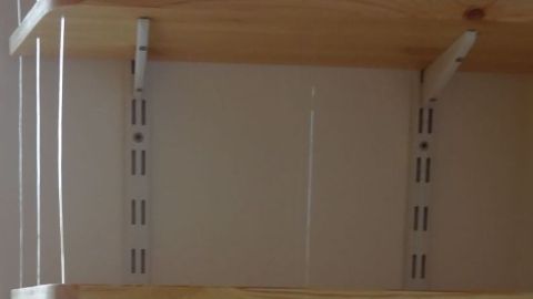 Ein offenes Bücherregal mit diskreten Seitenwänden bietet Platz für Bücher und Dekoration, umgeben von neutralen Wänden.