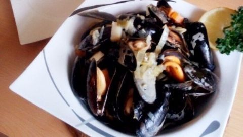 Miesmuscheln sind appetitlich in einer Schüssel angerichtet, garniert mit Zwiebeln und Zitrone, auf einem Holztisch.