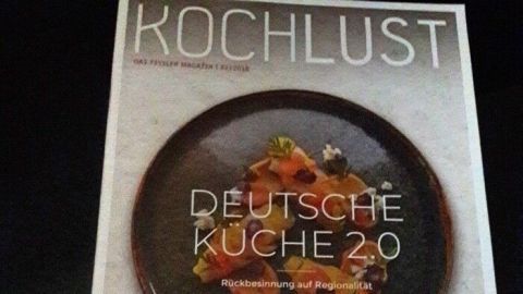 Eine Zeitschrift mit dem Titel "Kochlust" zeigt eine moderne deutsche Küche auf einem eleganten Teller mit frischen Zutaten.