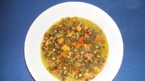 Ein Teller mit Grünkohleintopf, der dampfend vor einem blauen Hintergrund serviert wird, zeigt eine appetitliche Mischung aus Gemüse und Brühe.