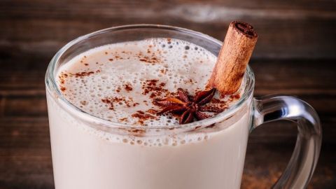 Ein Glas Chai-Tee mit Rum und Mandelmilch steht auf einem Holztisch, garniert mit Zimt und Sternanis.