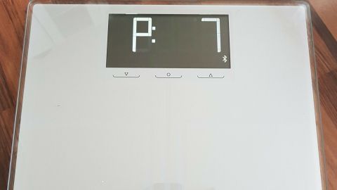 Eine digitale Waage liegt auf einem Holzboden und zeigt die Gewichtsanzeige P:7. Ideal für eine korrekte Gewichtskontrolle.