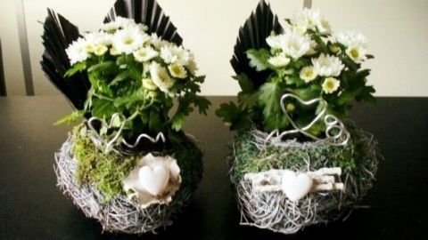 Zwei individuelle Grabgestecke mit weißen Blumen und Schwarz dekoriert, auf einem dunklen Tisch in einem ruhigen Raum platziert.