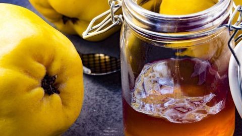 Gelbe Quitten liegen neben einem Glas mit goldenem Quittengelee auf einem dunklen Tisch, bereit zur Verwendung im Thermomix.