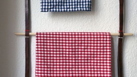 Ein Handtuchhalter aus alten Gürteln hängt an der Wand, während gestreifte Handtücher darauf hängen, um seine Funktion zu zeigen.
