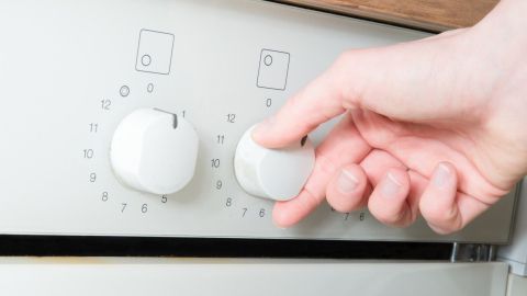 Eine Hand dreht den Regler eines Geräts, während das Küchenumfeld den Alltag begleitet und Marotten beim Kochen zeigt.