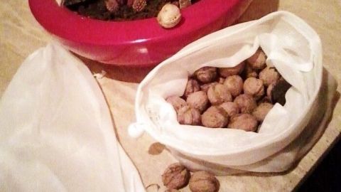 Eine weiße Tüte mit Nüssen wird auf einer Holzoberfläche abgewogen, während im Hintergrund eine dekorative Schale steht.