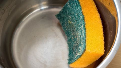 In einem glänzenden Topf liegt ein gelber und grüner Schwamm, bereit, um die eingebrannte Oberfläche zu reinigen.