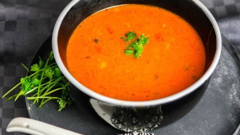 Eine schwarze Schüssel mit roter Aldi-Suppe steht auf einem dunklen Teller, umgeben von frischem Koriander.
