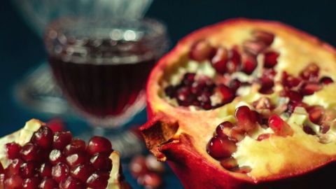 Ein halbierter Granatapfel liegt auf einem Tisch, aus dem rote Kerne und Saft fließen, umgeben von einem Glas Saft.