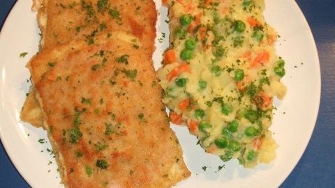 Auf einem weißen Teller liegen zwei Schinken-Käse-Schnitten neben buntem Kartoffelpüree, garniert mit Kräutern.