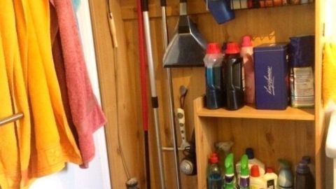 Ein Holzregal für Putzzubehör steht in einem Raum, beherbergt diverse Reinigungsmittel und Utensilien zur Aufbewahrung.