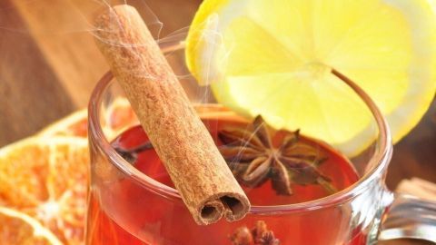 Ein Glas heller Glühwein mit Zimt und Sternanis steht auf einem Holztisch, umgeben von Zuckerstücken und Früchten.