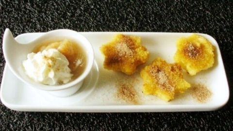 Süße, knusprige Kartoffelklöße liegen auf einem langen Teller neben einer Schüssel mit winterlichem Kompott und Sahne.