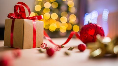 Ein hübsch verpacktes Weihnachtsgeschenk mit rotem Band liegt auf einem Tisch, umgeben von festlicher Deko und Lichtern.