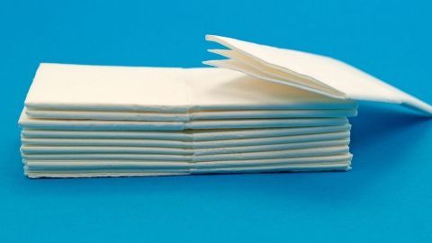 Im Vordergrund steht ein Stapel von Kärtchen, die zur Bekämpfung von Kleidermotten genutzt werden. Die Kärtchen liegen ordentlich übereinander auf einer blauen Unterlage.