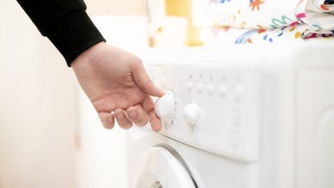Eine Hand stellt den Waschzyklus an einer Waschmaschine ein, während der Bezug des Beddinge-Schlafsofas gewaschen wird.