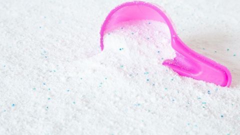 Ein rosa Messlöffel liegt in einem Haufen weißem Waschmittel, umgeben von einer hellen, neutralen Oberfläche.