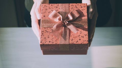 Ein schön verpacktes Weihnachtsgeschenk wird von zwei Händen gehalten, umgeben von einem minimalistischen, hellen Hintergrund.