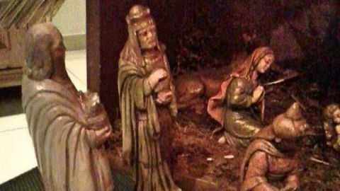 Krippenfiguren aus Gips stehen in einer Weihnachtskrippe, während eine Figur das Jesuskind hält und ein Kamel daneben steht.