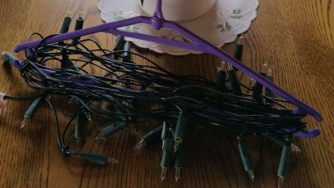 Eine Lichterkette ist ordentlich an einem Kleiderbügel aufbewahrt, während ein Weihnachtsstern in einem Topf auf einem Tisch steht.