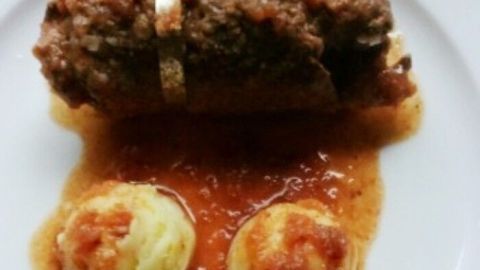 Rinderroulade liegt auf dem Teller, umgeben von Kartoffeln in Sauce, alles appetitlich angerichtet.