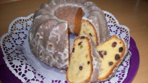 Ein Guglhupf auf Rührteig-Basis steht auf einer lila Platte und ist in Scheiben geschnitten, umgeben von einer Spitzenunterlage.